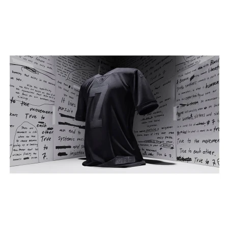 Black jersey with the number seven on display against a backdrop of white panels covered in handwritten text. Minimalist presentation.