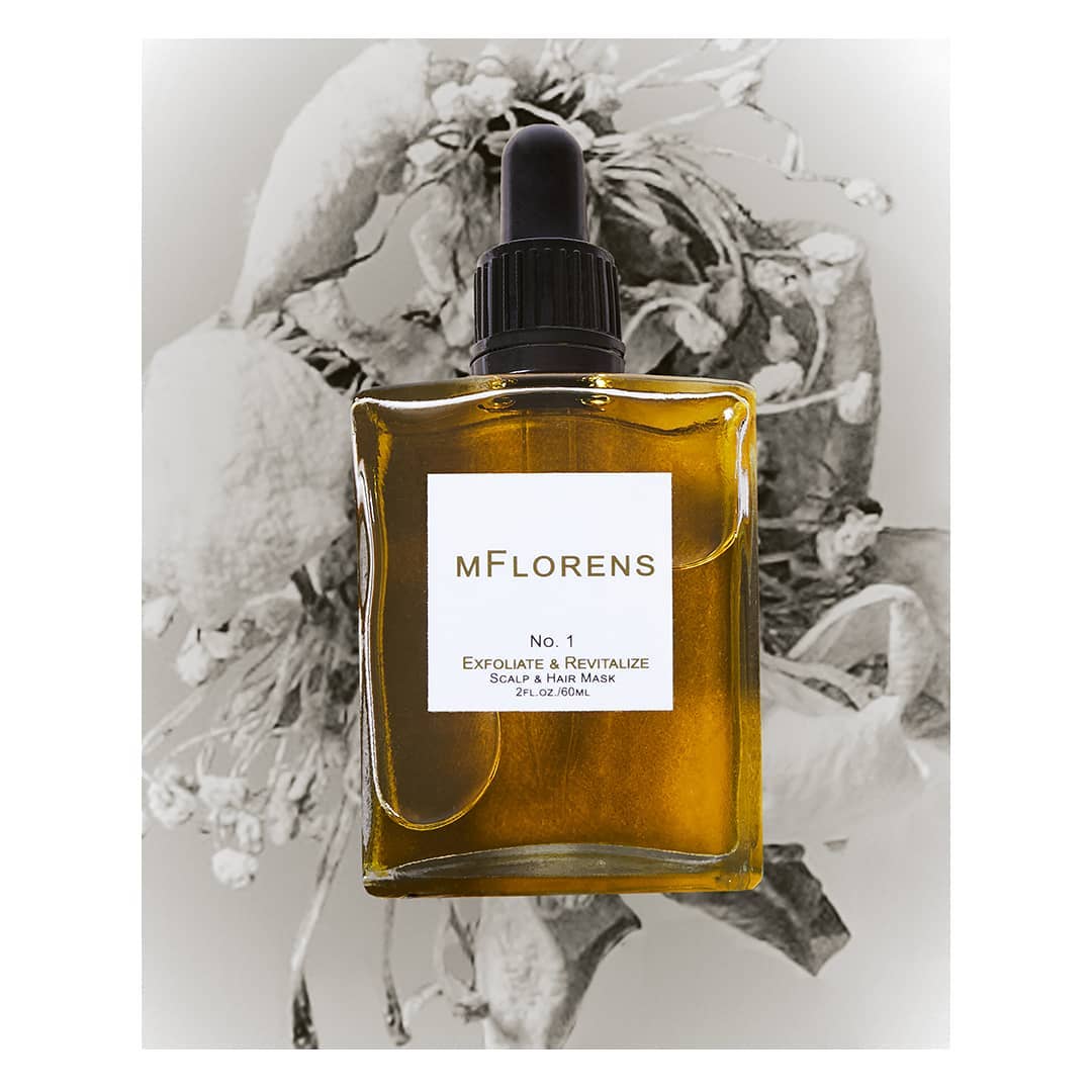 A bottle of MFlorens No. 1 Exfoliate & Revitalize Scalp & Hair Mask with a dropper cap, photographed in front of dried flowers.