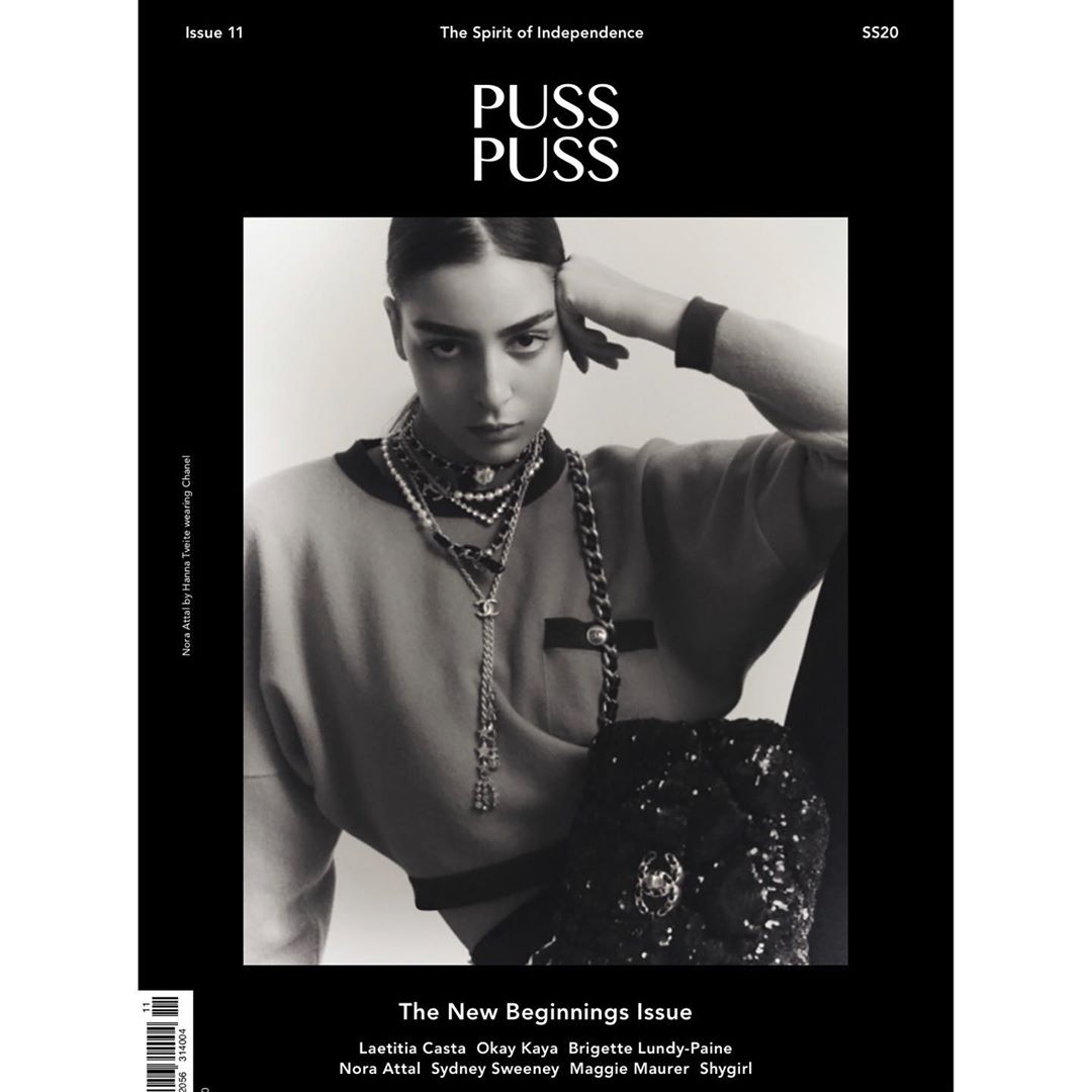Monochrome fashion magazine cover featuring a woman with layered necklaces, posing in a relaxed sweater with a dark, shiny shoulder bag.