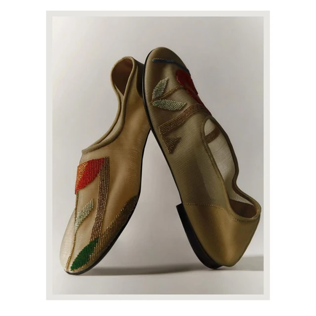 Two ornate, beige-toned slipper shoes with decorative beaded floral patterns on a light neutral background, positioned close together.