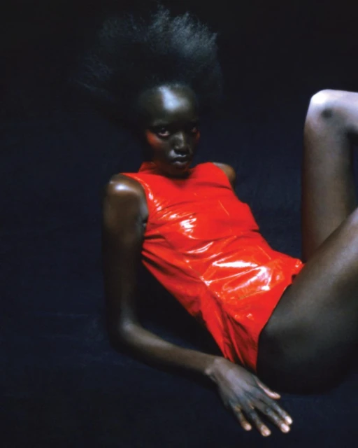 Woman with dark skin and high afro hairstyle poses in shiny red bodysuit against a dark background in studio lighting. Beauty and fashion.