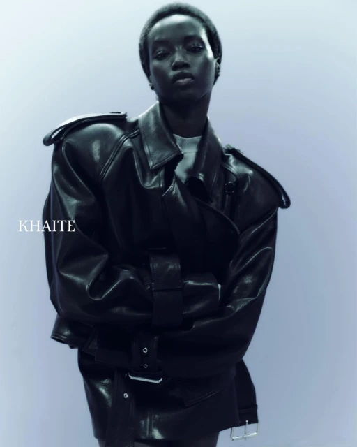 Close-up shot of an African American female model wearing a black leather jacket. Fashion shot with a plain backdrop, studio lighting.