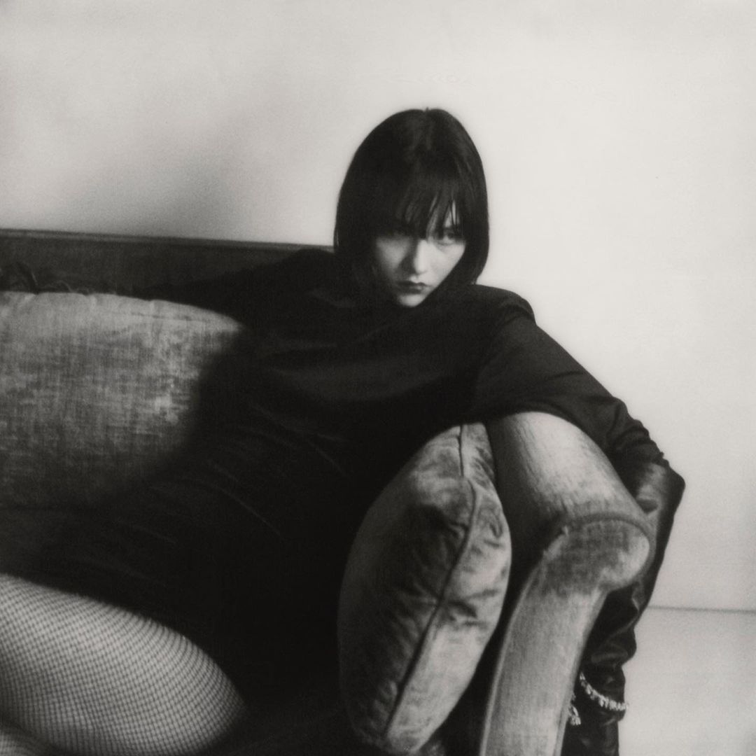 Woman in dark clothing seated on a sofa with pillows, photographed by Hanna Tveite in New York.