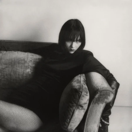 Woman in dark clothing seated on a sofa with pillows, photographed by Hanna Tveite in New York.