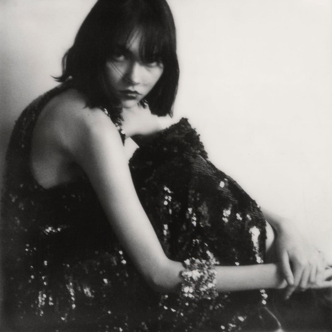 Portrait of a woman wearing a dark sequined dress seated against a plain light background