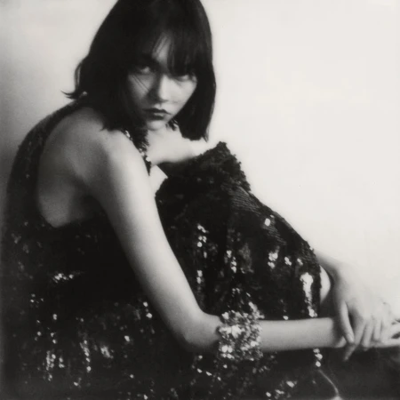 Portrait of a woman wearing a dark sequined dress seated against a plain light background