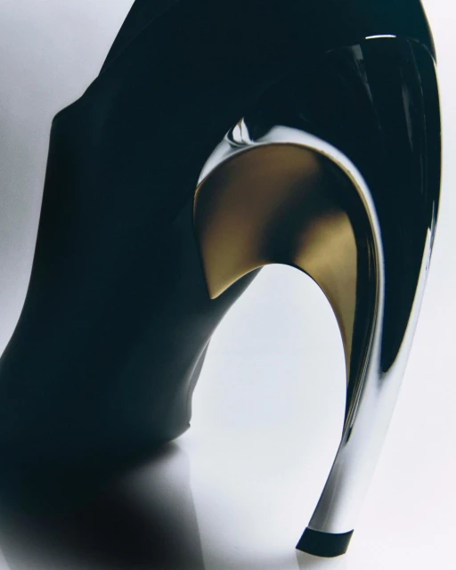 Elegant black high-heel shoe featuring a unique, reflective silver and gold curved heel design, presented on a clean white background.