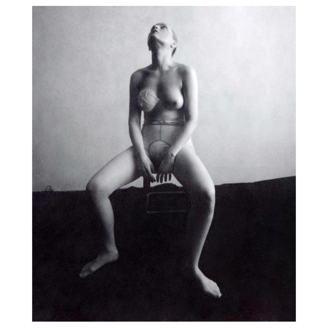 Black and white image of a seated adult woman in undergarments looking up, captured in an indoor setting with neutral background.