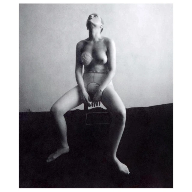 Black and white image of a seated adult woman in undergarments looking up, captured in an indoor setting with neutral background.