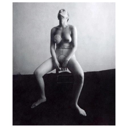 Black and white image of a seated adult woman in undergarments looking up, captured in an indoor setting with neutral background.