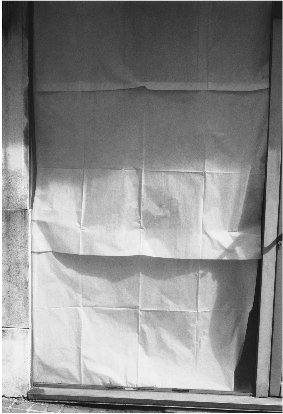 Black and white shot of a doorway covered with draped white fabric, blocking view and obscuring details of the door and the surrounding wall.