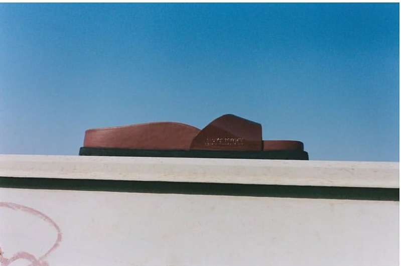 Studio shot of a brown sandal on a white surface against a clear blue sky. Minimalist product photography.