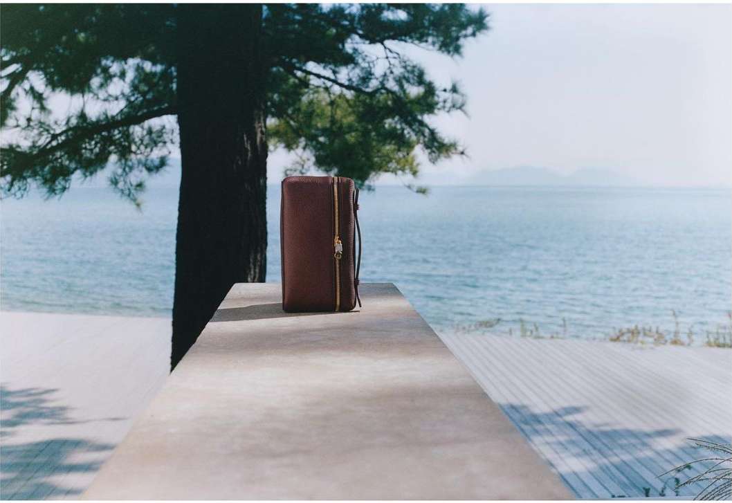 Brown leather wallet with zipper on concrete table overlooking the ocean with a tree. Minimalist product shot for fashion accessory.