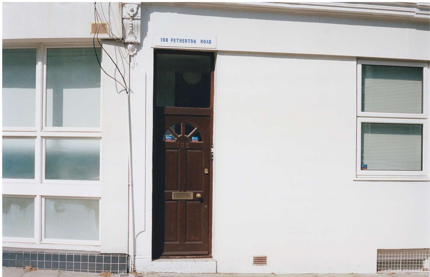 Exterior view of a building with a brown door and white facade, featuring windows and the street address '108 Petherton Road'.