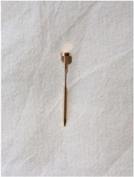 A sleek gold metal pen resting vertically on a textured off-white fabric background with a soft circular highlight.