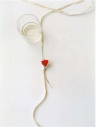 Overhead shot of a red fabric rose pinned to a pale ribbon next to a glass of water on a white surface.