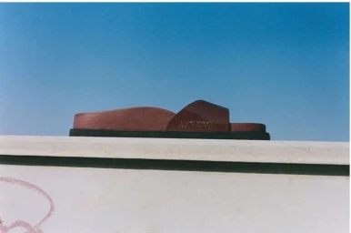 Brown sandal resting on a light ledge against a clear blue sky background