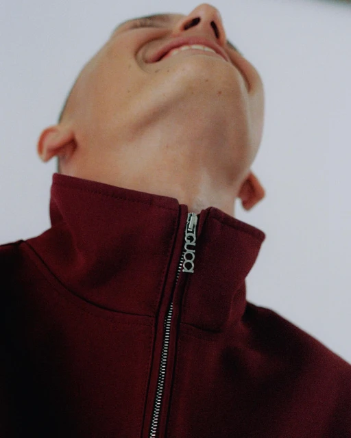 Portrait of a man looking up with a burgundy jacket, showing the jacket zipper with the 'booda' logo, against a white background.