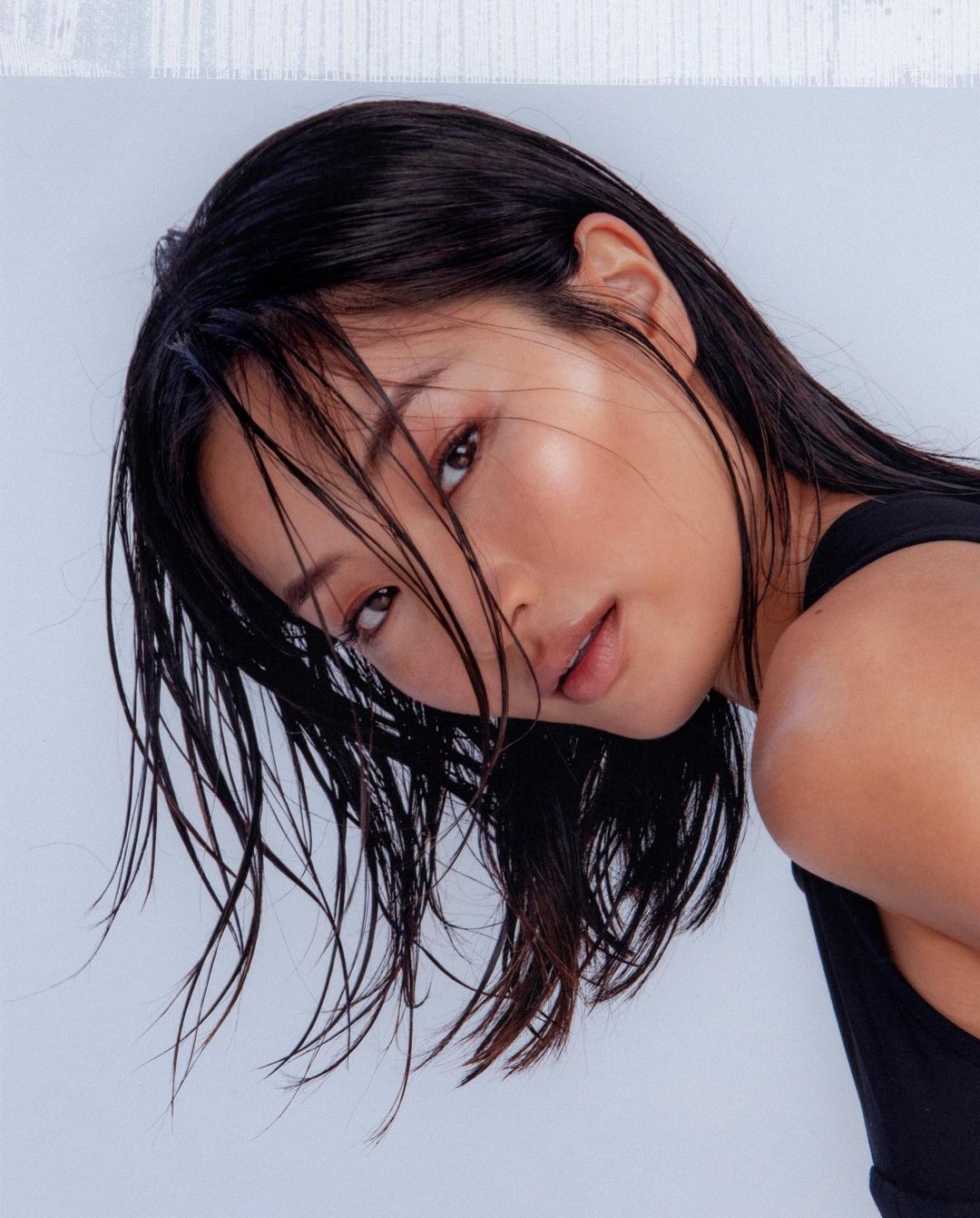 Close-up portrait of a beautiful adult female with dark hair and fair skin, wet hair strands on her face, wearing a black top.