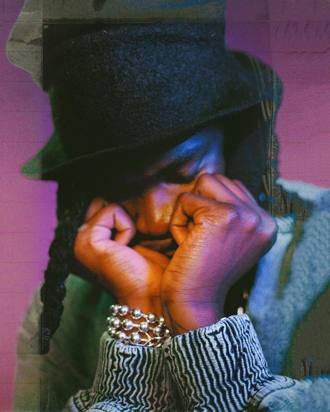 Portrait of a person wearing a dark bucket hat and beaded bracelet with hands under chin, captured by Hannah Sider