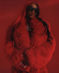 Portrait of a woman wearing a red faux fur coat and black sunglasses against a monochromatic red background