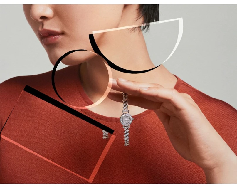 Elegant studio shot showcases a woman wearing an orange top, elegantly presenting a silver wristwatch adorned with diamonds. 