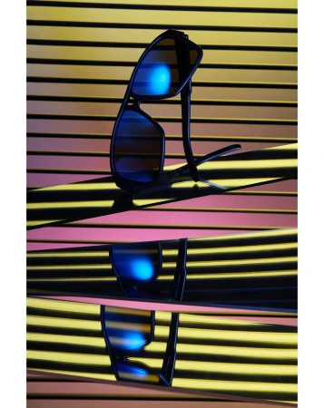 Black sunglasses with blue tinted lenses resting on angular mirrored surfaces against a striped yellow and pink background.