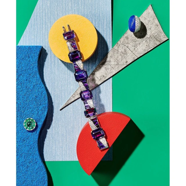 High-angle product shot of a purple gem bracelet and ring, arranged on geometric shapes against a colorful background.