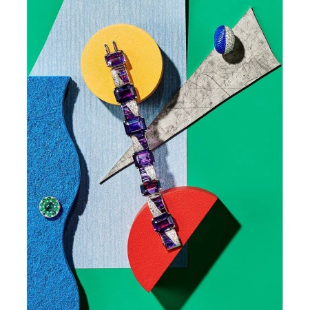 High-angle product shot of a purple gem bracelet and ring, arranged on geometric shapes against a colorful background.
