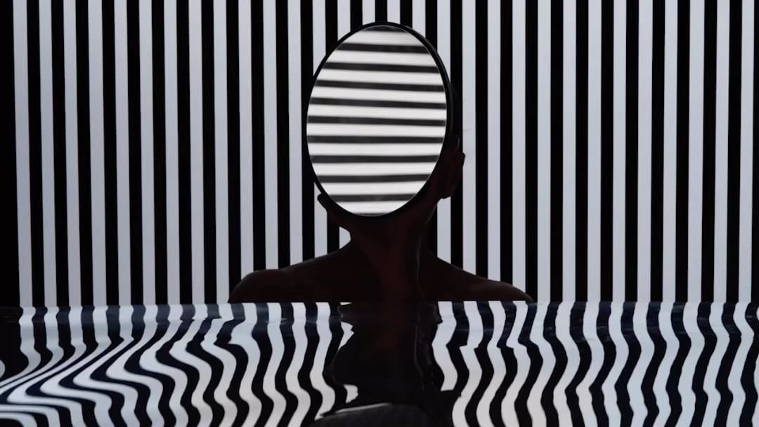 Abstract portrait of a human silhouette holding a round mirror with black and white stripe reflections against a matching stripe background.