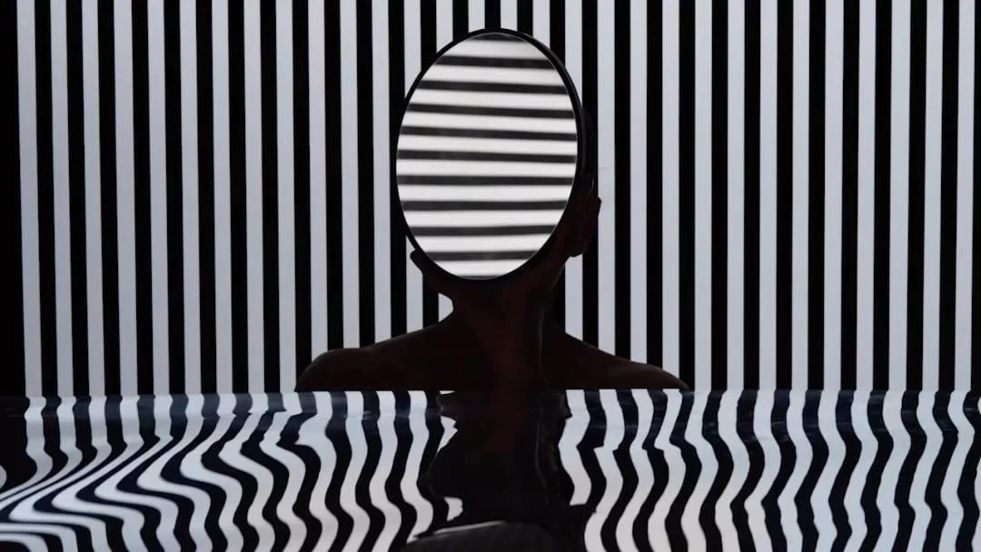 Abstract portrait of a human silhouette holding a round mirror with black and white stripe reflections against a matching stripe background.