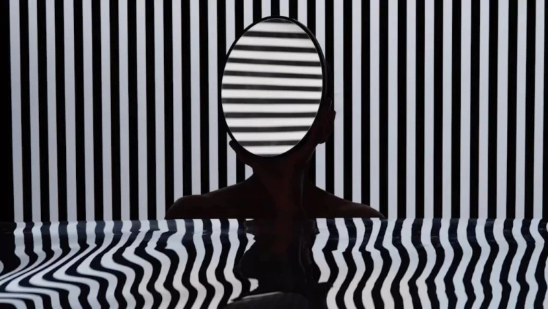 Abstract portrait of a human silhouette holding a round mirror with black and white stripe reflections against a matching stripe background.