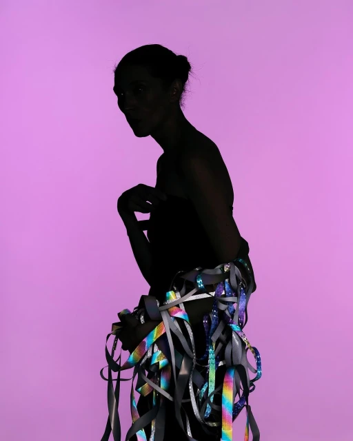 Silhouette of a woman wrapped in iridescent ribbons against a lavender background, creating a striking visual with dynamic lighting.