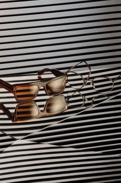 Still life of two pairs of eyeglasses on a reflective surface with a black and white horizontal striped background. Fashion and beauty.