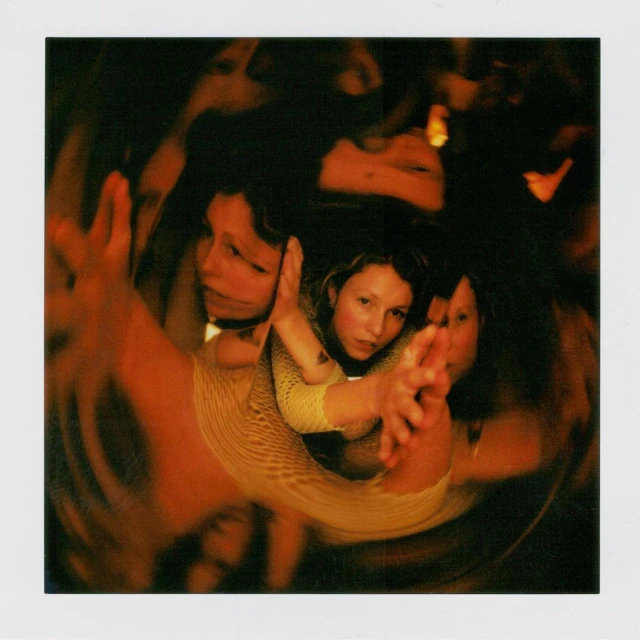 Abstract portrait with warm lighting. A woman faces the camera, with blurred, reflected faces and arms encircling her in the image.