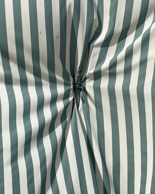 Striped fabric with teal and white vertical stripes, gathered in the center with a black plastic buckle creating a textured pattern.