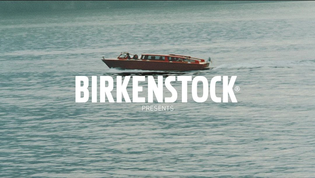Red water taxi speeds across teal water in a video for Birkenstock, the brand's logo in white is centered over the boat.