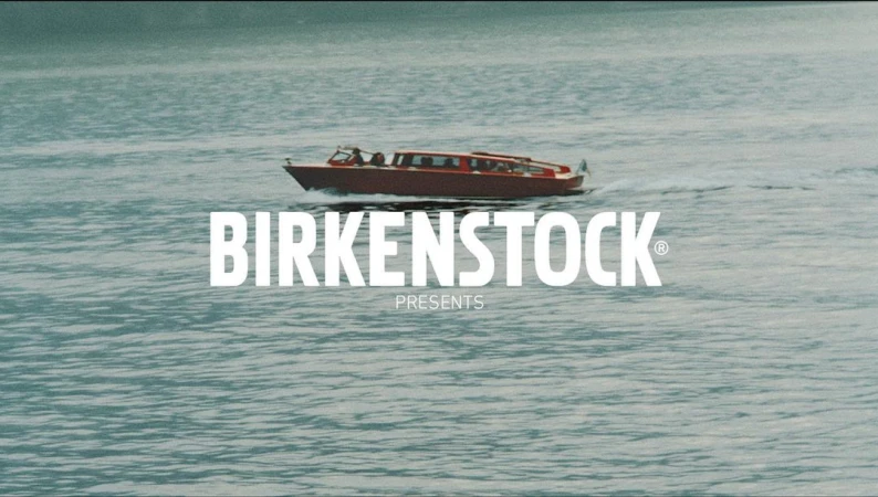 Red water taxi speeds across teal water in a video for Birkenstock, the brand's logo in white is centered over the boat.