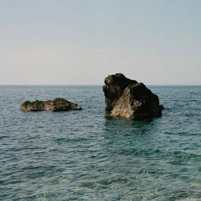 Two large rocks are surrounded by water in this outdoor landscape. The scene is captured in natural light on a clear day.