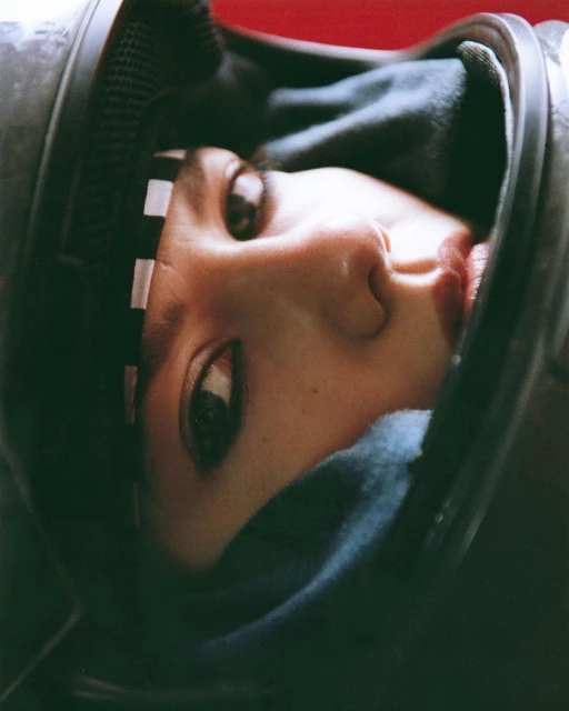 Close-up portrait of a person wearing a dark helmet against a red background, facing slightly upwards into the camera lens.