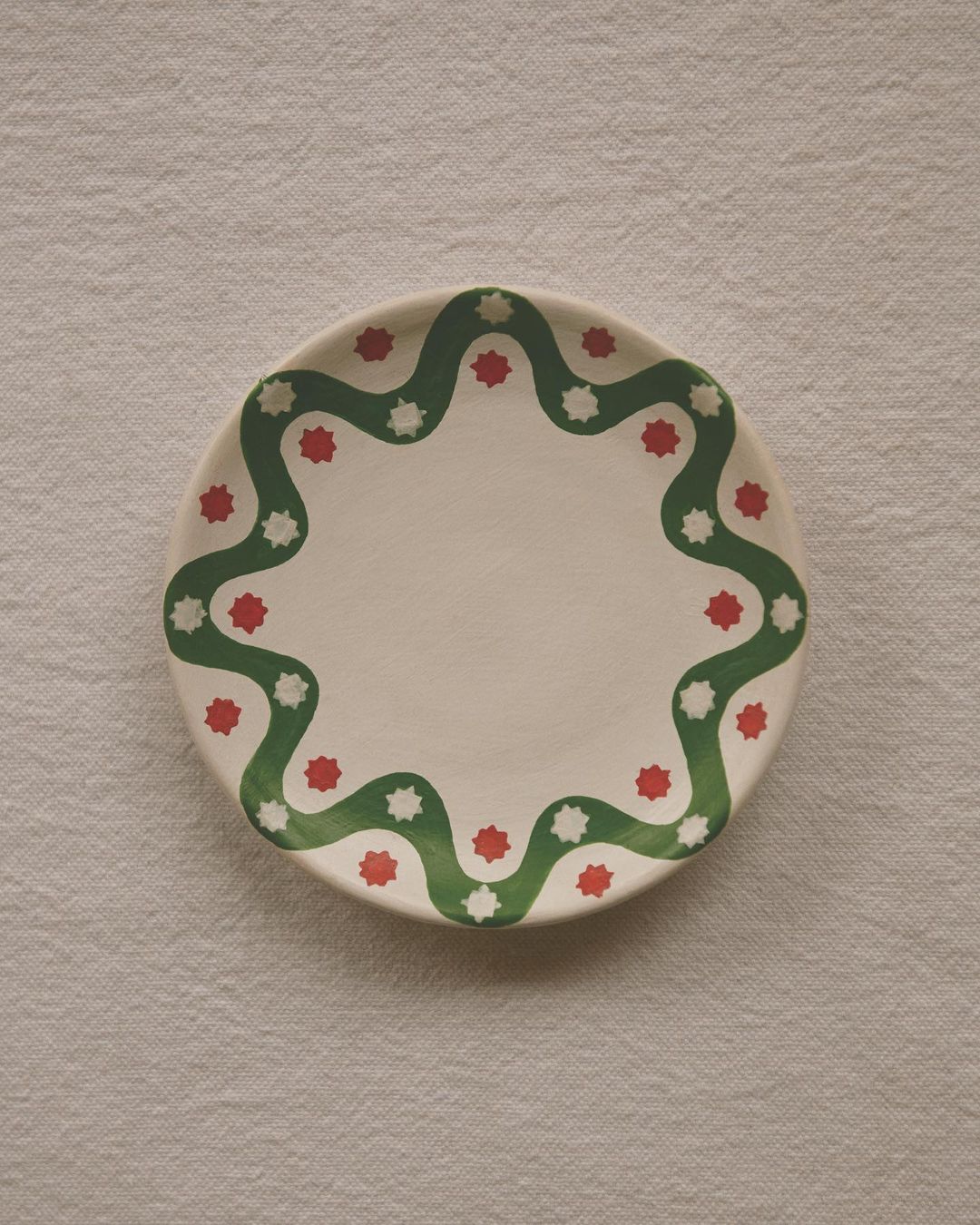 Overhead shot of a white ceramic plate with a green wavy pattern and red and white star shapes arranged on a textured white cloth.