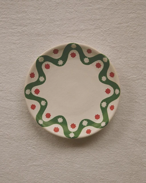 Overhead shot of a white ceramic plate with a green wavy pattern and red and white star shapes arranged on a textured white cloth.