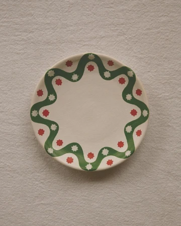 Overhead shot of a white ceramic plate with a green wavy pattern and red and white star shapes arranged on a textured white cloth.
