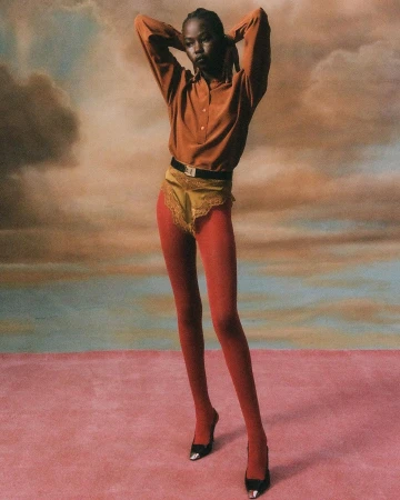 Model in rust shirt and red tights posing against a painted cloud backdrop by Hans Neumann