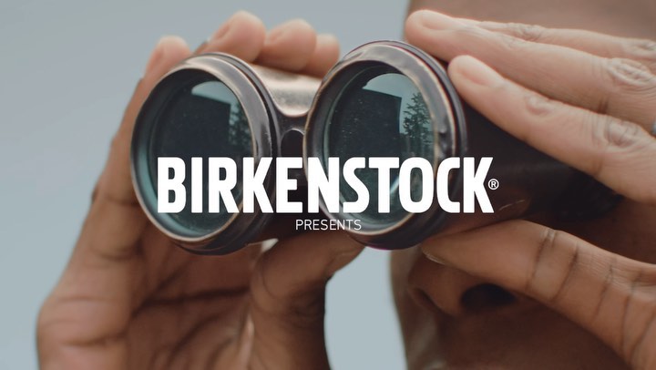 Close-up of an adult using binoculars, with the brand name BIRKENSTOCK and the word PRESENTS visible in a marketing image.