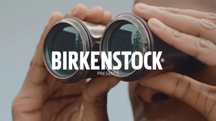 Close-up of an adult using binoculars, with the brand name BIRKENSTOCK and the word PRESENTS visible in a marketing image.