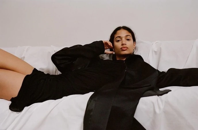 Woman in a black satin shirt and shorts reclining on a white sofa, photographed by Hans Neumann