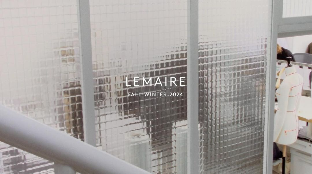 Fashion brand Lemaire Fall-Winter 2024 promotion displayed on a frosted glass window, with garment on a dress form visible.
