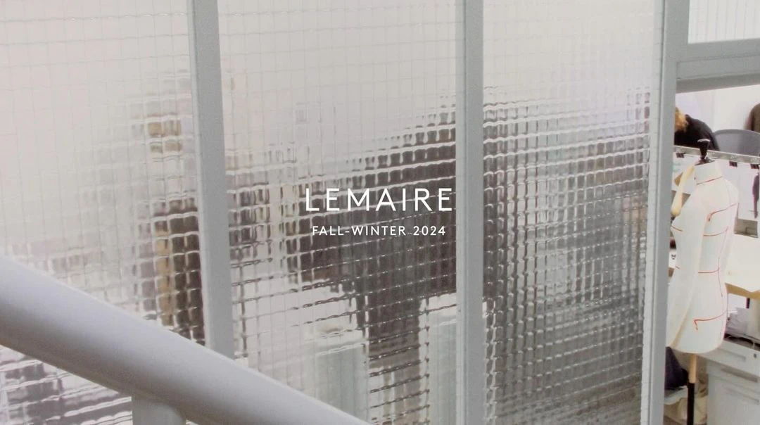 Fashion brand Lemaire Fall-Winter 2024 promotion displayed on a frosted glass window, with garment on a dress form visible.