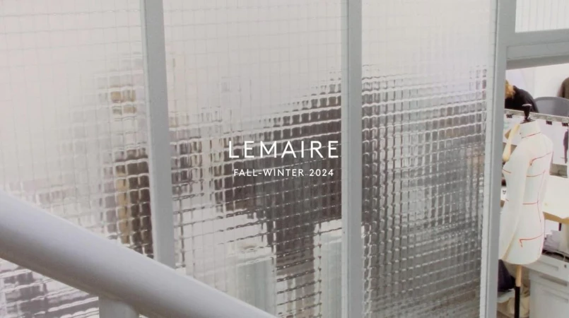 Fashion brand Lemaire Fall-Winter 2024 promotion displayed on a frosted glass window, with garment on a dress form visible.